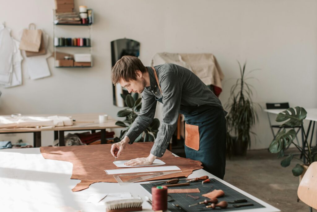 A craftsman designs and cuts leather in a sunlit workshop, showcasing handmade artistry.